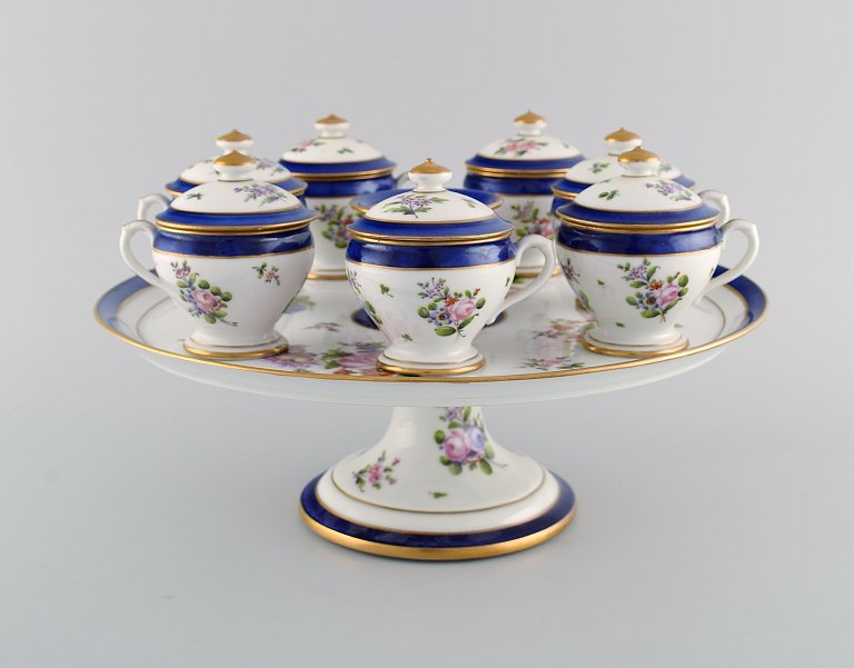 Sevres, Frankrig. Syv antikke cremekopper på opsats i håndmalet porcelæn med blomster og gulddekoration. 1800-tallet. 